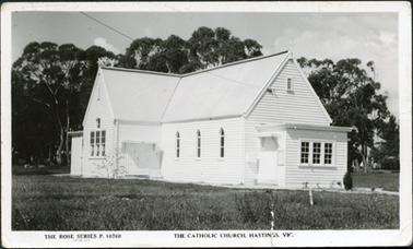 This is an image of the Catholic Church in Hastings. The church is a weatherboard building in pristine condition with lawn all around.  Large trees are in the background.  Printing on the bottom of the postcard is as follows: “The Rose Series P.10760  The Catholic Church, Hastings. Vic”. 