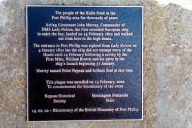 This image is a photograph of a large square grey plaque attached to a stone.  The inscription is as follows: “The people of the Kulin lived in the Port Phillip area for thousands of years.  Acting Lieutenant John Murray, Commander of HMS Lady Nelson, the first recorded European ship to enter the bay, landed on 14 February 1802 and walked out from here to the high dunes.  The entrance to Port Phillip was sighted from Lady Nelson on 4 January 1802 but the ship did not attempt entry of the Heads until 14 February following a survey by the First Mate, William Bowen and his party in the ship’s launch beginning 31 January.  Murray named Point Nepean and Arthurs Seat at this time.  This plaque was unveiled on 14 February, 2002 To commemorate the bicentenary of the event  Nepean Historical Society Morning Peninsula Shire 14.02.02 - Bicentenary of the British Discovery of Port Phillip”.