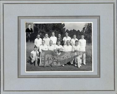 This image shows a group of cricket players, in two rows, posing for a photo.  There are seven men standing in the back row and six sitting in the front row.  The player on the far left-hand side of the image is sitting on his haunches.  The man in the centre of the back row is searing a three-piece suit and tie and all other men are wearing whites.  The two players on each end of the front row are holding cricket bats.  The player in the centre of the front row is wearing cricket gloves.  A large banner is stretched out across the front row and reads: “BCC Premiers 1945-6”.  A small photo of a man wearing a dark coat, white shirt and tie is inserted into the top left-hand corner of the photograph.  There are grass and tall trees in the background.  