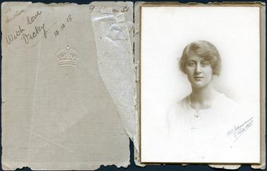 This image is of a portrait of a young woman taken from the chest up. She  is wearing a white square necked top and has a fine chain around her neck.  Her hair is swept up and pinned at the back.  The photographers details are written across the bottom left-hand side of the photograph.  The photograph is mounted on board and glued into a brown paper cover.  A royal crown is embossed on the front of the cover and the photographers details are printed in brown ink .  