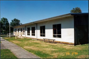 This image shows a long flat-roofed, white timber building.  Several sets of windows are across the front of the building.  A ramp and a flag pole can be seen behind a white sign on the grass, which reads; “Hastings-Western Port Historical Society”.  Grass and a concrete footpath are in the foreground and trees can be seen on the left-hand side of the photograph.  Three posts with a rail is close to the building.  The date the photo was taken is stamped on the lower right-hand corner.