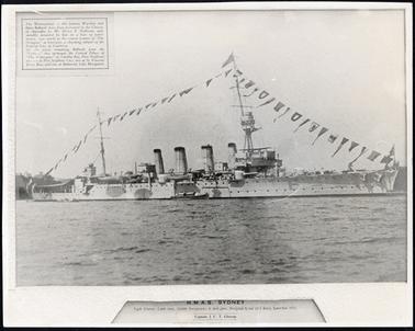 This image shows the H.M.A.S Sydney in port.  The ship has four large funnels and a line of flags flowing from end to end supported by two tall masts.  There is a large expanse of water in the foreground.  There is a small boat along side the ship.  Printed on the mounting beneath the image is information about the ship and the action on 9th November, 1914..  There is also information in small print in a text box in the top left-hand corner of the photograph.  