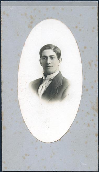 This image is an oval portrait of a young man taken from the chest up.  He is wearing a white shirt with a very high turned-up collar and a tie.  His hair is neatly combed with a part on the left side.  He has a slight smile on his face and is looking slightly away from the camera.  