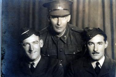 This image shows the top section of three men in military uniform posing for a photograph.  The two men at the front appear to be sitting and the man behind them appears to be standing and leaning forward.  The two men at the front are wearing similar uniforms, shirt,ties and coats with airforce caps.  The man at the back is wearing a heavy jacket, buttoned up to the neck and a large cap.  