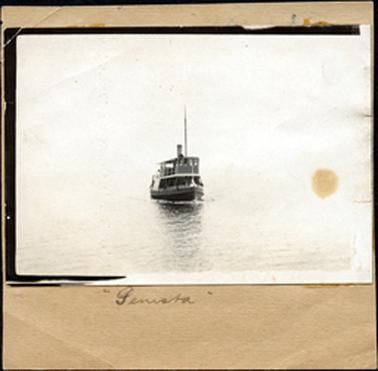 This image shows a boat on the water coming towards the camera.  There is no background.  Written on the paper at the bottom of the photograph is: “Genista”. 