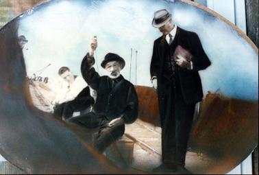 Colour photo of an oval shaped painting.  From left to right a seated man in a white shirt with a pipe in his mouth; a seated man in a black outfit and hat holding a line in his hand; man standing dressed in a suit hat and tie. Appears the men are on a wooden pier or wharf with a crane in the far background.