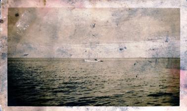 This badly marked sepia image shows a boat/yacht at the centre of a large expanse of water.
