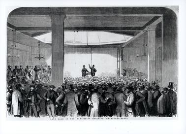 This is a photograph of a sketch. The backs and the heads of a large number of men are facing the front where two men are standing conducting a sale.  The building has large pillars and light pendants are hanging from the ceiling.  Printed across the bottom of the image is: “Land Sale in the Exhibition Building Melbourne. - See Page 7”.