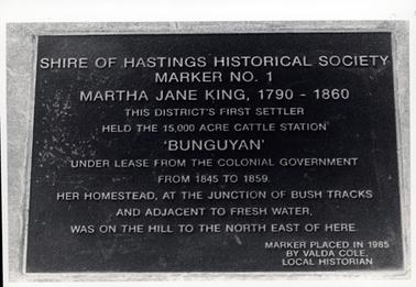 This image shows a metal plaque attached to stone.  The plaque reads: “Shire of Hastings Historical Society Marker No. 1 Martha Jane King, 1790 - 1860 This district’s first settler held the 15,000 acre cattle station ‘BUNGUYAN’ under lease from the Colonial Government from 1845 to 1859.  Her homestead, at the junction of bush tracks and adjacent to fresh water, was on the hill to the north east of here.  Marker placed in 1985 by Valda Cole, Local Historian.  