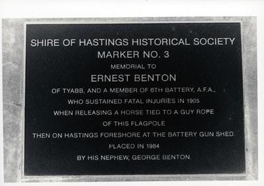 This image shows a metal plaque attached to stone.  The plaque reads: “Shire of Hastings Historical Society Marker No. 3 Memorial to Ernest Benton of Tyabb, and a member of 6th Battery, A.F.A., who sustained fatal injuries in 1905 when releasing a horse tied to a guy rope of this flagpole then on Hastings foreshore at the Battery Gun Shed.  Placed in 1984 by his nephew, George Benton.”