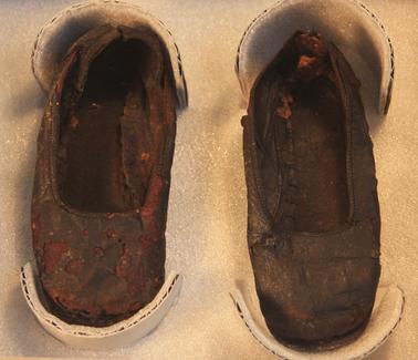 Pair of children’s leather shoes.  Upper section of each shoe is composed of several pieces of brown leather.  Soles and heels made of leather.  Straps have been lost.  (Refer to Treatment Report for full description)