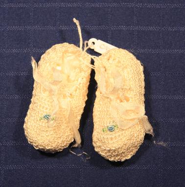 White crocheted baby booties.  Blue “grub rose” on top of each one threaded with white ribbon.
