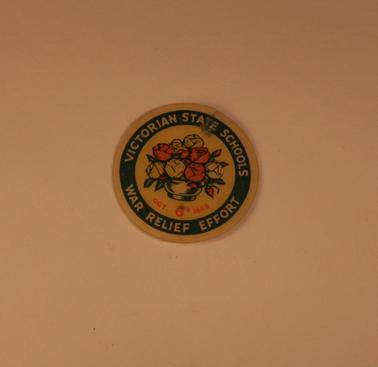 Victorian State School War Relief Effort Badge October 1943.  2.5cm round cardboard covered with celluloid , with vase of roses -yellow background, printing on green background