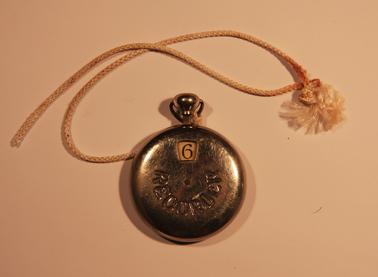 Round metal container with button to press to show a number in small window.  Numbers up to 8 ‘Recorder’ stamped into case.  Piece of white cord attached to ring on button.