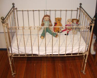 Child’s cast Iron cot.  Originally white. Brass knobs on each corner.  Drop down sides.  Wire mattress base.