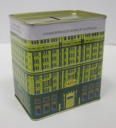 Tin money box in the shape of a building, with windows and doors denoted. Yellow and green in colour with Commonwealth Bank of Australia in gold lettering on white background at top of box.