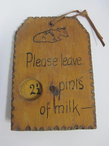 Piece of 3 plywood with circular piece attached to back with screw. The words “Please leave ......  pints of milk”  Circular hole cut into wood and when circle is turned, printed quantities appear.  