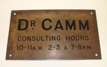 Brass Doctor’s shingle with black printing “Dr Damm Consulting Hours 10 - 11.00A.M, 2-3 and 7-8 P.M”.  Four screw holes.