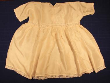 White baby’s silk dress.  Lace insert at waist and lace trim on bottom.  Crocheted around neck and edge of sleeves.  Hand worked designs