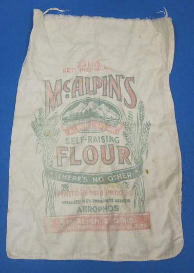 Calico bag, rectangular in shape, with opening at top of short side.  “McALPINE’S SELF RAISING FLOUR” logo in red and green printing.  “25 Lbs nett when packed” in red printing.  “J. McAlpin & Sons, Abbotsford, Melbourne Phone JA 3126” in red rectangle at bottom. 