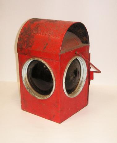 Red painted kerosene lamp.  Square with dome top.  Access door and handle.  “Advance” on dome top.  Access door inscribed:  CHALWYN TRAFFIC SIGNS RG. 40. REGO. DESIGN 965446 7.  BS 3143 PART 1 