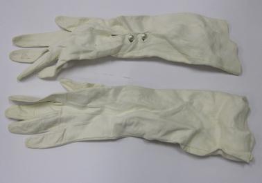Long white kid evening gloves with opening at wrist area, fastened by two imitation pearl buttons.