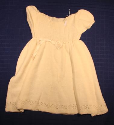Plain knitted white woollen dress with ribbon tie under arms.

