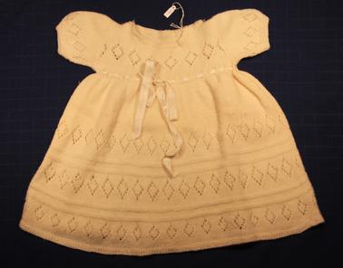 White woollen baby dress, first size.  Threaded ribbon around dress at underarm 
