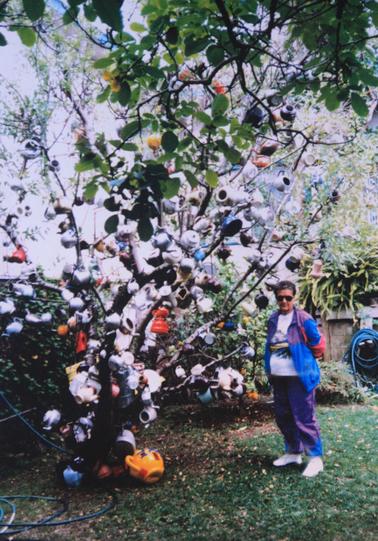 A4 copy of photo tree with numerous tea-pots of varying kinds. Edie Cameron by side of tree.