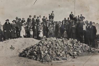 Rye townspeople behind pile of bricks in 1927.  Many ladies in long dresses, younger ones in knee length.  Men in suits. Most in crowd wearing hats.  Boys wearing caps.  Centre front facing to her right - Mrs A Hunt, Owner of the Gracefield Hotel.