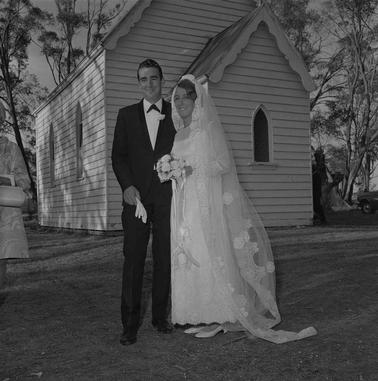 A bride and groom in front of a weatherboard church building.