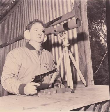Man in a shelter shed with a gun looking through a telescope.