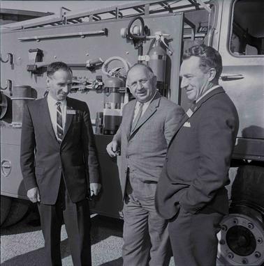 Three men in suits posing near a firetruck.