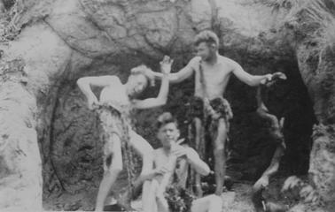 Merricks Beach Cavemen. Three men horsing around in the cave at Merricks Beach. Dressed in seaweed (?) skirts. Two standing, one has the other by the hair. Thick twisted tree limb in other hano date. Other seated, has stick to mouth.