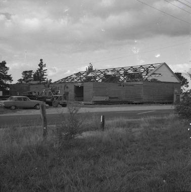 A large weatherboard shed without a roof cover.  A car and small crane are parked nearby.