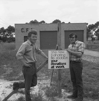 Two men leaning on a sign in front of the Balnarring Fire Station.