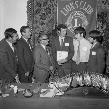 Six menbehind a table  gathered in front of a Lions club banner.