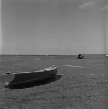 Tidal flats with a marooned dinghy, a water channel in in the distance.