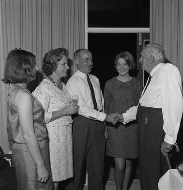 Two men shaking hands while three women look on.