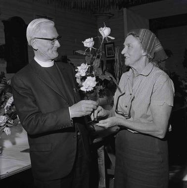 A clergyman and a fwoman inspecting an arrangement of roses.