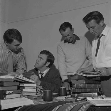 Four men checking stacks of books pile don a table and chatting.