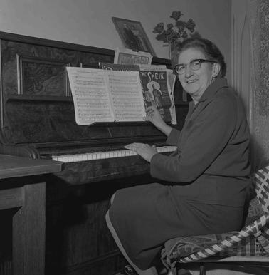 A woman seated at a piano which haswith an open musi book on the book bracket. 