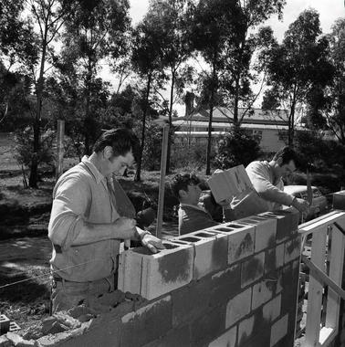 Two men laying a cement brick wall.