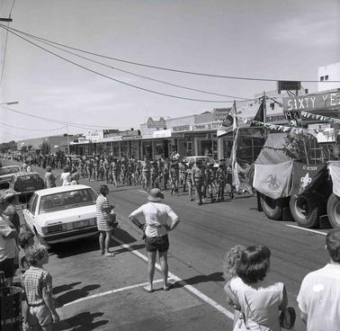 A business street scene with Scouts marching behind a float.