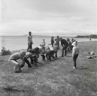 A line of people at a Bayside foreshore, crouching down to pick up a tug of war rope. A few others looking on.