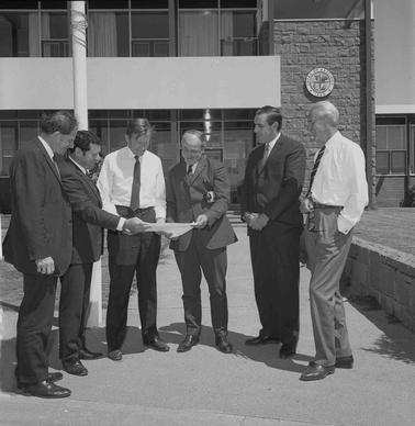 Six men in business clothes inspecting a document.