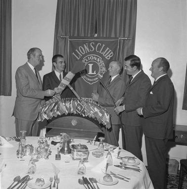 Five men standing behind a set dinner table, gathered in front of a Lions Club banner.