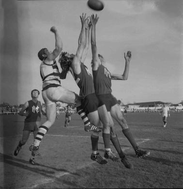 Three footballers jumping for a ball.