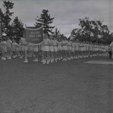 Two long rows of school children in sports uniform with a school banner.
