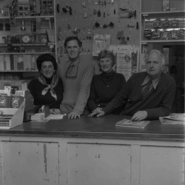 Two women and two men posing behind a general store counter.